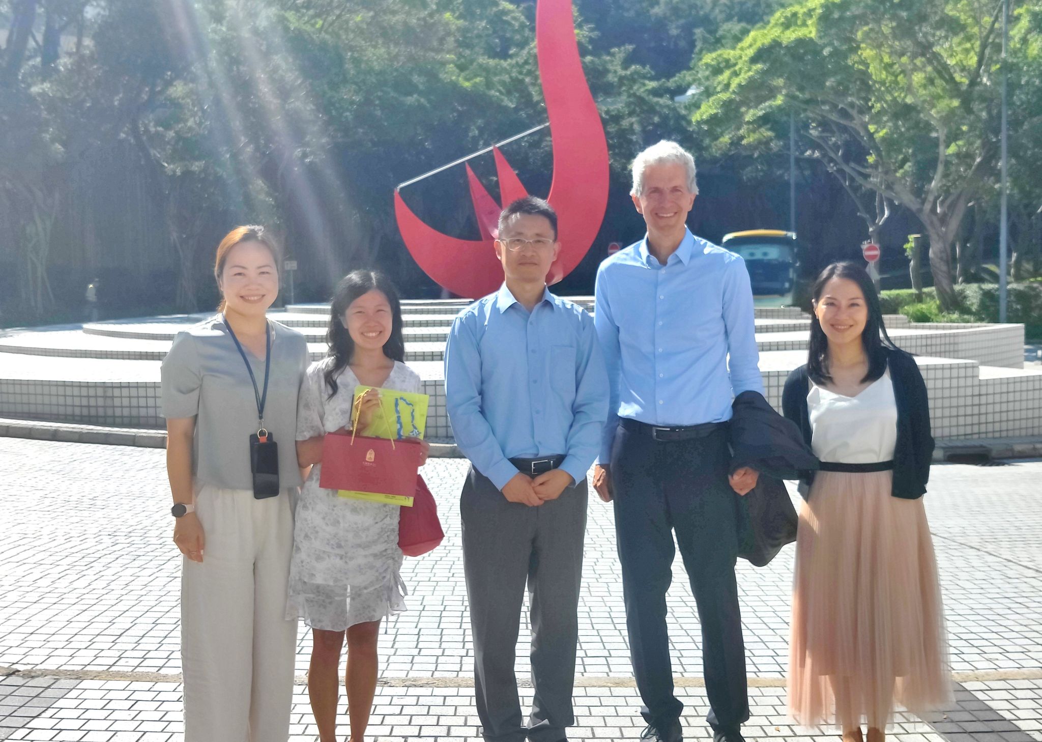 A group photo of Consul General Stefan BREDOHL (second right) and the HKUST team in front of the iconic “Red Bird” sculpture at the Piazza.