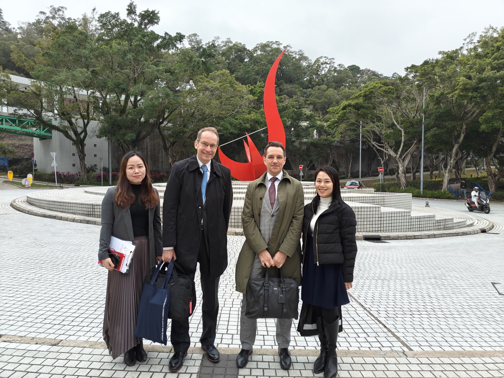 A group photo featuring Dr. Andreas GÖTHENBERG (second left) and Dr. Erik FORSBERG (second right) alongside the HKUST team, taken in front of the iconic "Red Bird" sculpture at the Piazza.