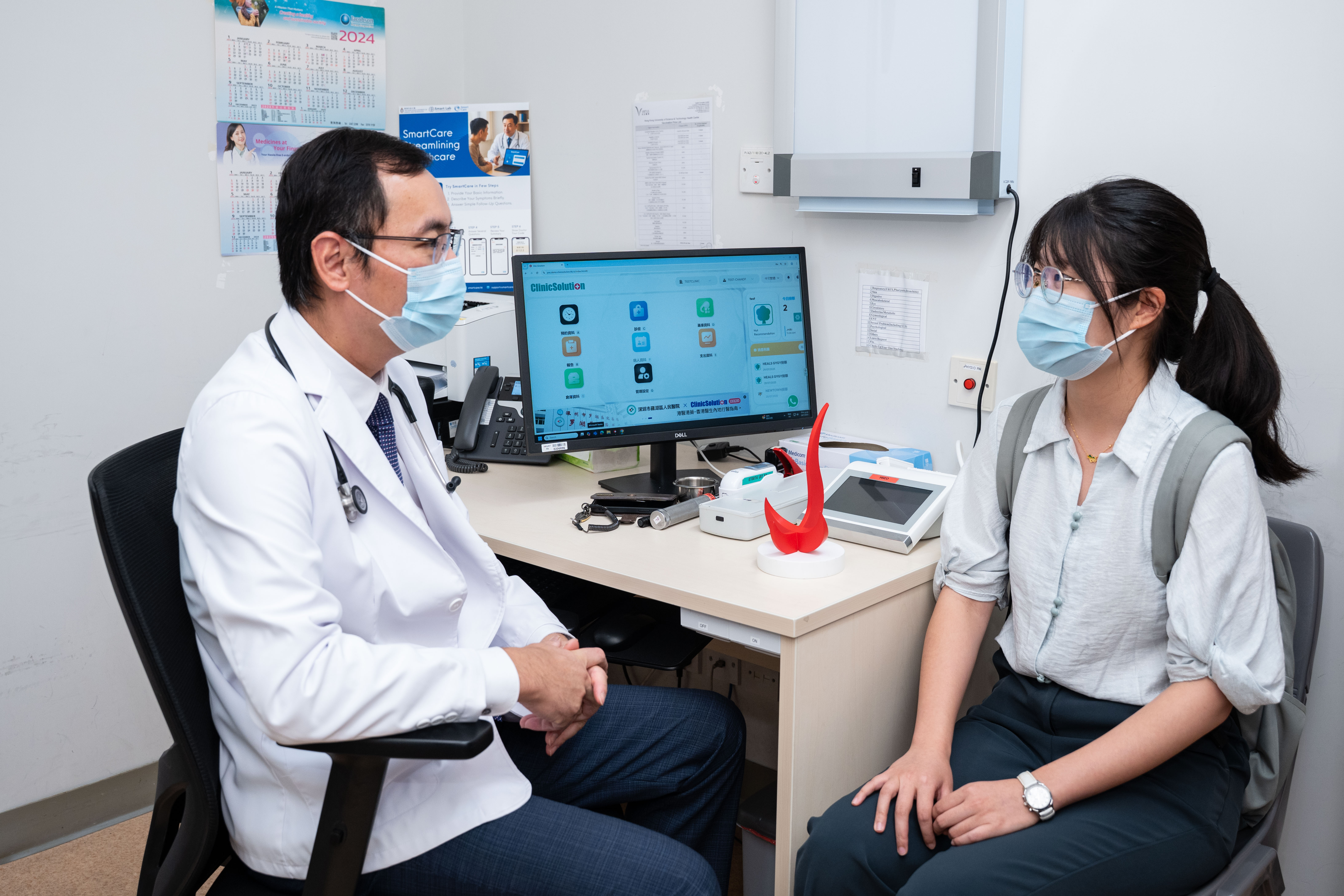 为期六个月的SmartCare先导计划，邀请科大全体师生及校内人员参与体验并提供意见。有份开发SmartCare的郑毅诚医生（左）同时亦是科大医疗中心执业的注册西医，图片为他正模拟使用系统协助诊症的流程。