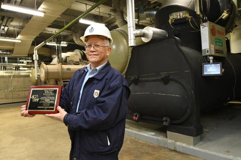  科大校園設施管理處副處長林乾禮先生於一台新的製冷機組前展示獎項。