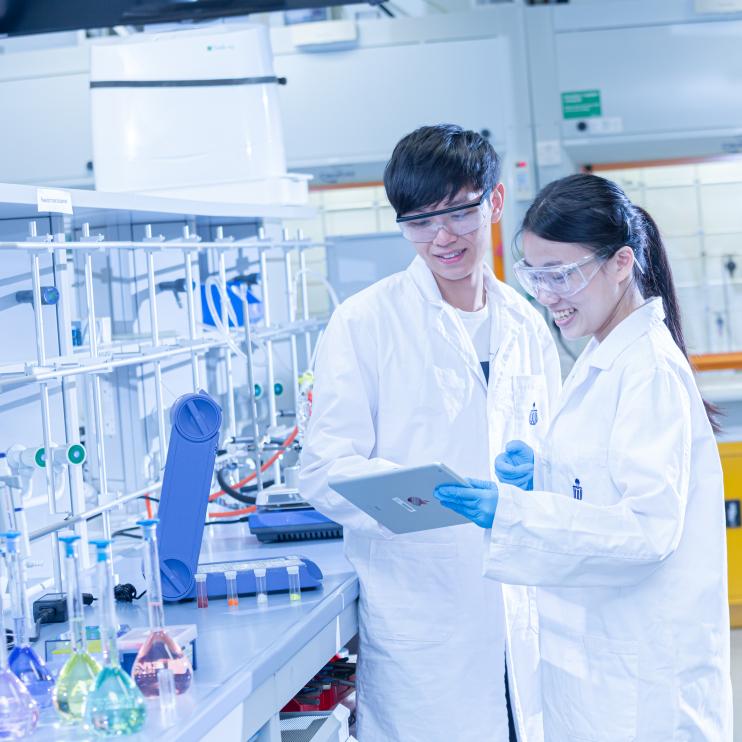 2 people wearing HKUST lab coats inside a science lab